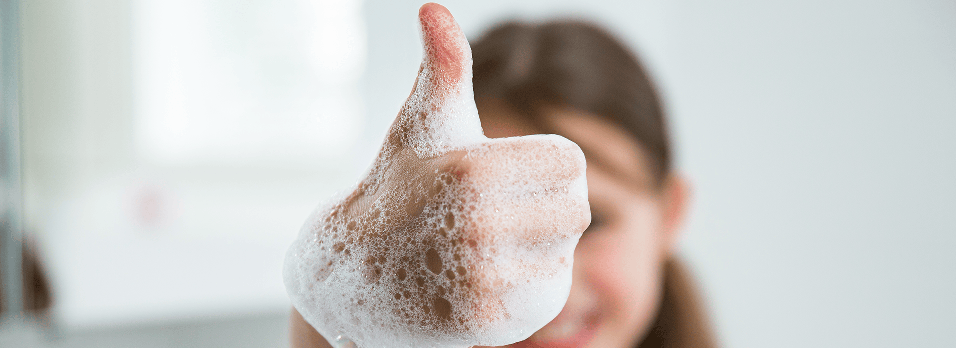 Kind zeigt die Geste "Daumen hoch". Die Hand ist voller Seifenschaum.