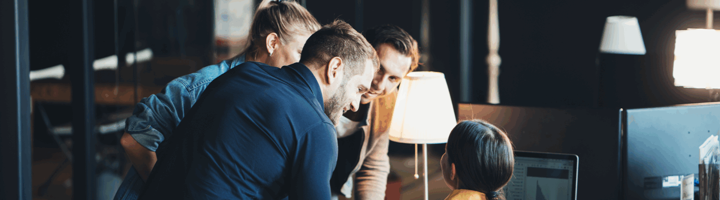 Personen, die um einen Schreibtisch herum stehen und sich unterhalten.