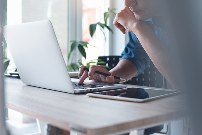 Mann sitzt vor einem Laptop, eine Hand ist auf der Tastatur.