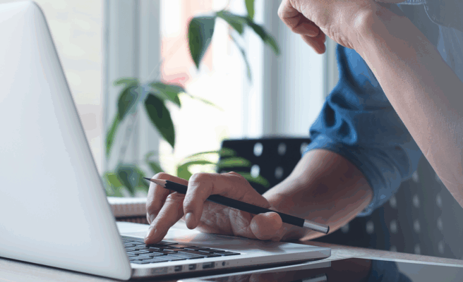 Mann sitzt vor einem Laptop, eine Hand ist auf der Tastatur.