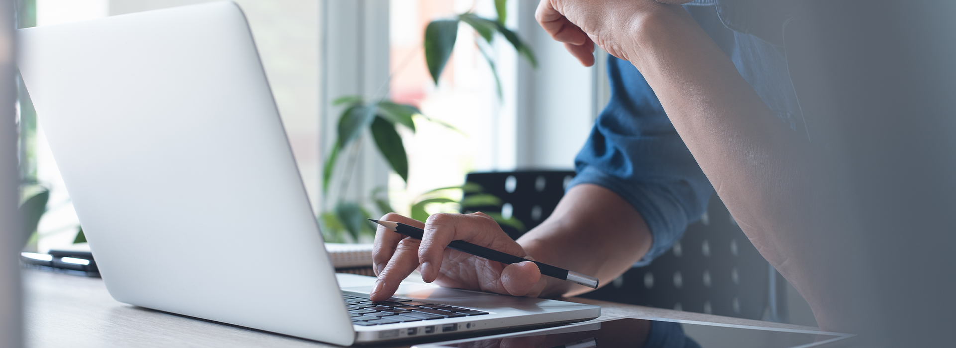 Mann sitzt vor einem Laptop, eine Hand ist auf der Tastatur.