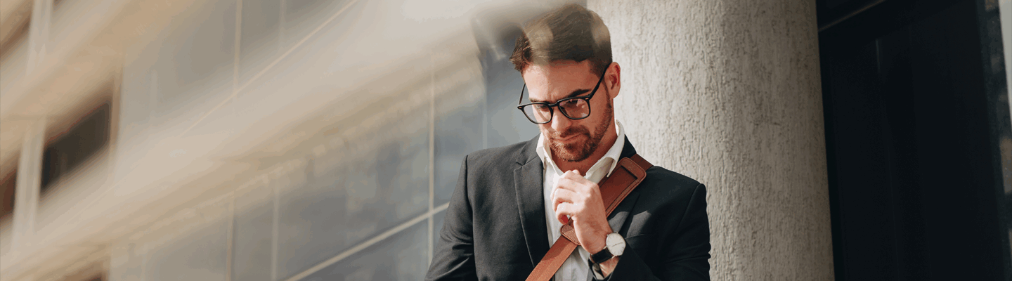 Mann, Business Casual, lehnt an einer Hauswand und schaut auf sein Handy - Brunata Minol Connect hilft bei der Fernablesung