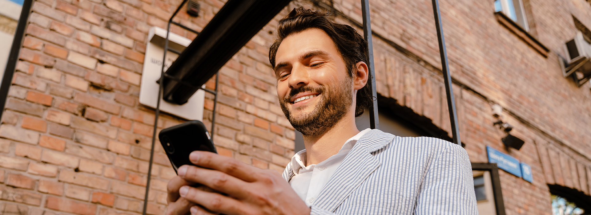 Mann schaut lächelnd auf ein Smartphone in seinen Händen