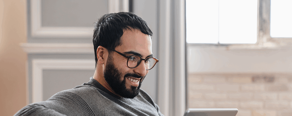 Mann sitzt auf einem Sofa und schaut etwas auf seinem Tablet an, das er in den Händen hält.