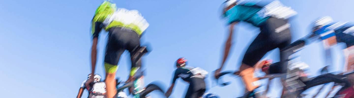 Aufnahme eines Radrennens. Man sieht professionelle Radfahrer etwas verschwommen von hinten.