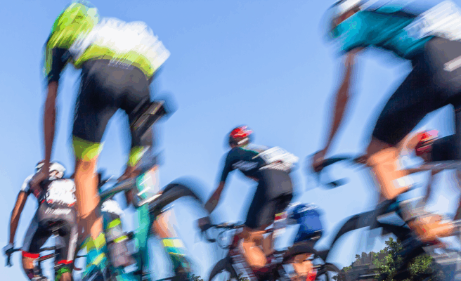 Aufnahme eines Radrennens. Man sieht professionelle Radfahrer etwas verschwommen von hinten.