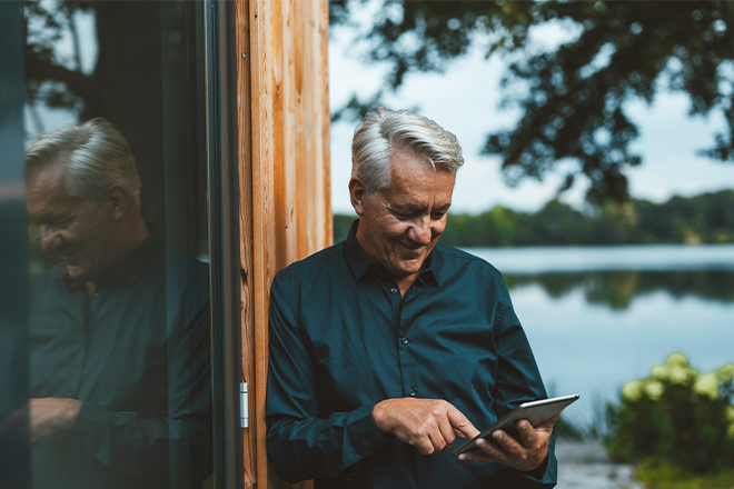 Mann lehnt an einer Hauswand und schaut auf ein Tablet, das er in seinen H&auml;nden h&auml;lt. Nat&uuml;rliche Umgebung.