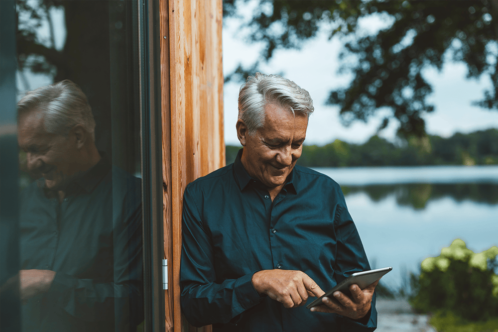 Mann lehnt an einer Hauswand und schaut auf ein Tablet, das er in seinen Händen hält. Natürliche Umgebung.