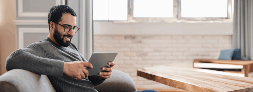 Mann sitzt auf einem Sofa und schaut etwas auf seinem Tablet an, das er in den Händen hält.