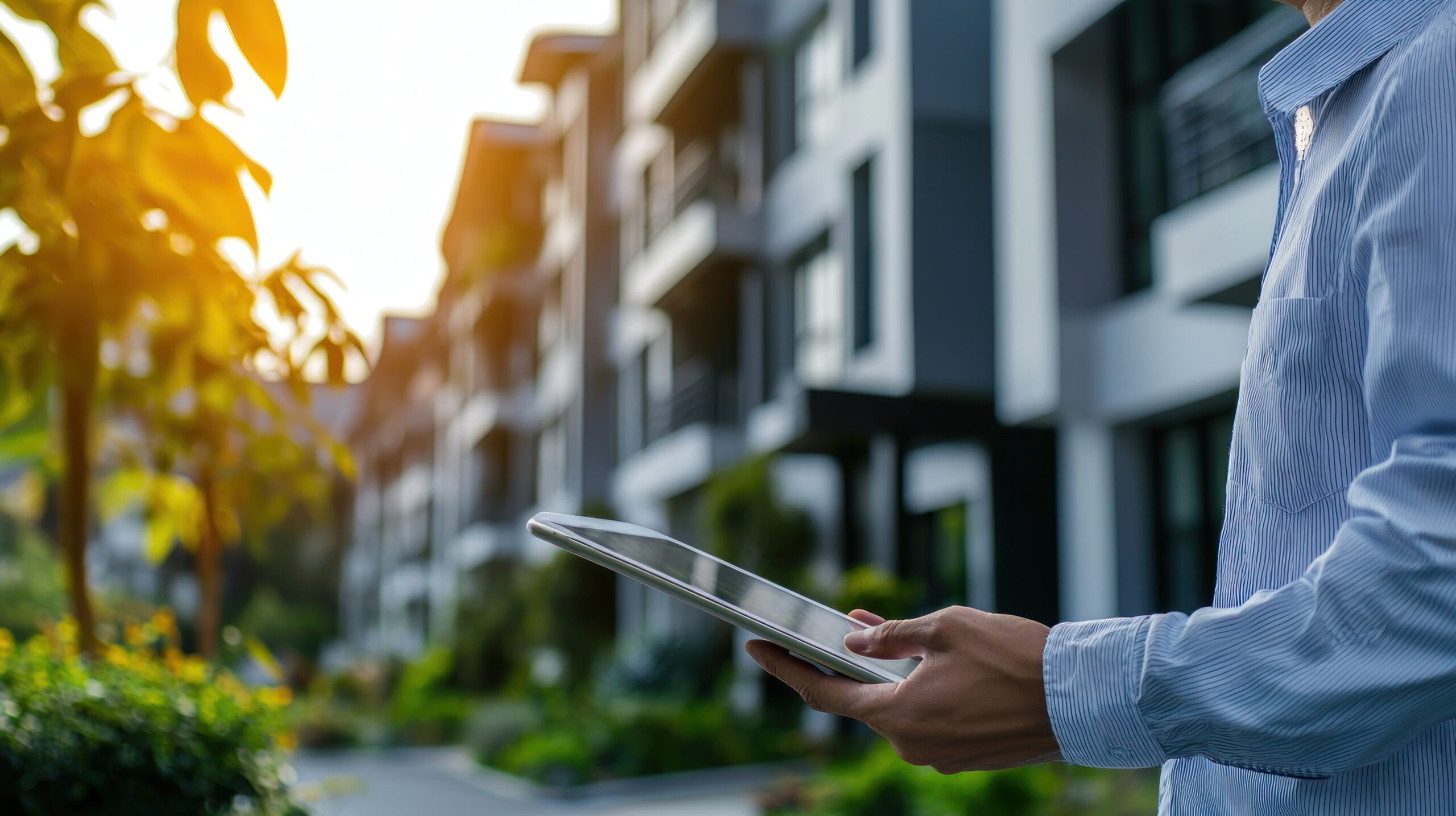 Wohnungswirtschaft. Mann steht vor Mehrfamilienhäusern mit Tablet